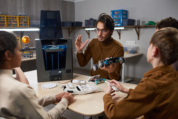 Portrait of young male teacher demonstrating 3D printing technology to diverse group of children in robotics class at school