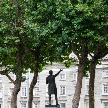 Eine Statue unter Bäumen mit erhobener Hand vor einem großen Gebäude in Dublin