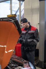 Fototapeta na wymiar Vertical portrait of male mechanic inspecting engine while working in car repair shop
