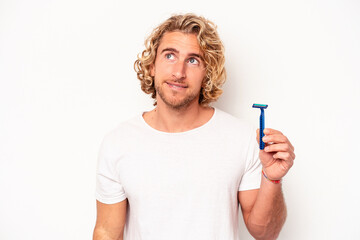 Young caucasian man shaving his beard isolated on white background dreaming of achieving goals and...