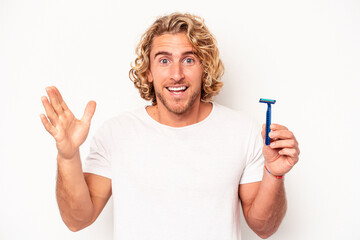 Young caucasian man shaving his beard isolated on white background receiving a pleasant surprise,...