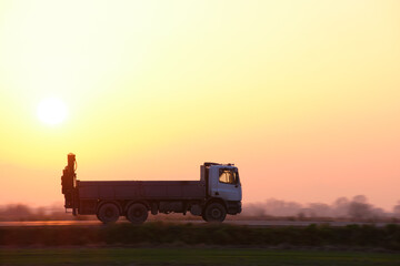 Cargo dump truck driving on highway hauling goods in evening. Delivery transportation and logistics...