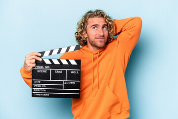 Young caucasian man holding a clapperboard isolated on blue background touching back of head, thinking and making a choice.