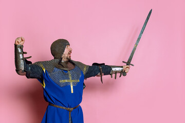 Portrait of brave man, medieval warrior or knight in armor rising sword, showing readiness to fight...