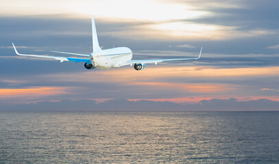 Airplane flying over tropical sea at sunset