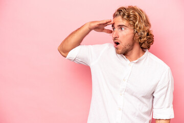 Young caucasian man isolated on pink background looking far away keeping hand on forehead.