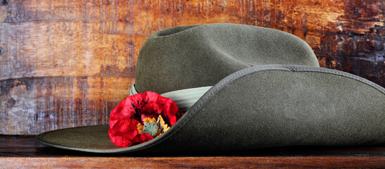 Australian army slouch hat on dark recycled wood with remembrance red poppy for Anzac Day or Remembrance Armistice Day. Sized to fit popular social media and web banner placeholder. - obrazy, fototapety, plakaty