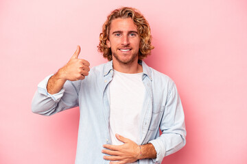 Young caucasian man isolated on pink background touches tummy, smiles gently, eating and...