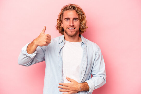 Young caucasian man isolated on pink background touches tummy, smiles gently, eating and satisfaction concept.