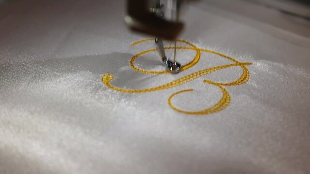 Machine embroider the inscription "B" on a white satin robe. Inscription bride with golden thread. Wedding day preparation. Elegant bridal lingerie. Close up. Full Hd Video.	