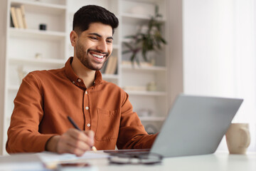 Portrait of smiling Arab man using laptop and writing