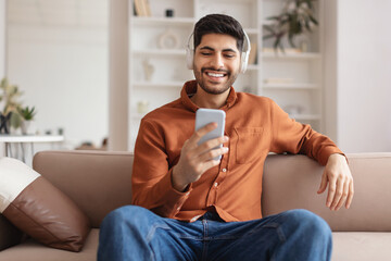 Smiling bearded man in wireless headhones using cellphone - obrazy, fototapety, plakaty