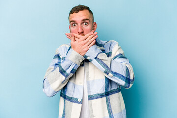 Young caucasian man isolated on blue background covering mouth with hands looking worried.