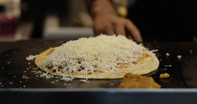 Closeup shot of a Chef making Vegetable Frankie, Kathi Roll, Veg Franky Wrap. Grating cheese adding sauces, potato filling, spices, cabbage salad on Indian flat bread. Mumbai, Maharashtra, India. 4810