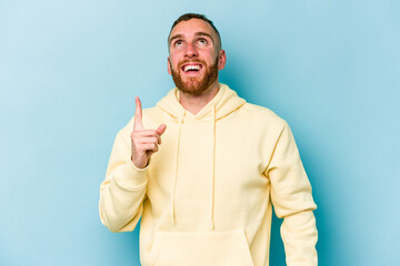 Young caucasian man isolated on blue background indicates with both fore fingers up showing a blank...