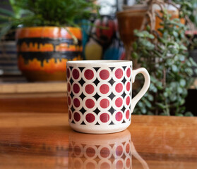 Mid-century modern porcelain cup with spray painted pattern on a wooden table, with plants in the background