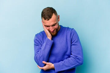 Young caucasian man isolated on blue background laughs happily and has fun keeping hands on stomach.