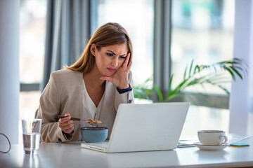 A woman in the office eats at work. Laptop at the table. She is at her workplace. , a glass of water and coffee in the background. The concept of lunch at work and healthy food.