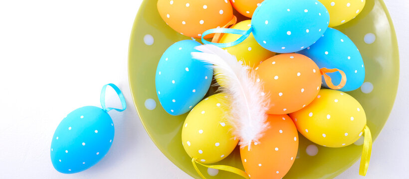 Happy Easter bright blue, yellow and orange polka dot Easter Eggs on green plate on white wood background. Sized to fit popular social media and web banner.