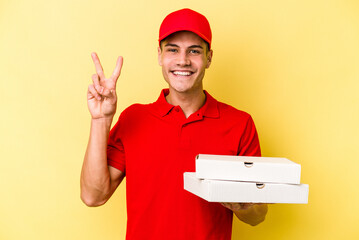 Young delivery caucasian man holding pizzas isolated on yellow background showing number two with fingers.