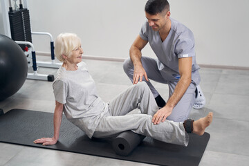 Therapist adjusting aging female leg on roll for exercise