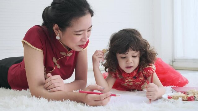 Asian young mother is teaching her little daughter to drawing in the room.