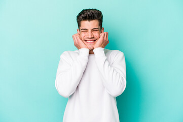 Young caucasian man isolated on blue background covering ears with hands.