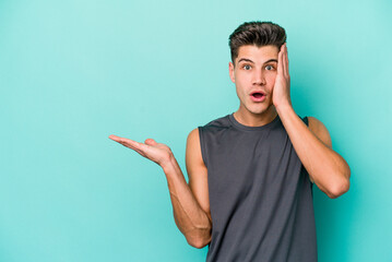 Fototapeta premium Young caucasian man isolated on blue background impressed holding copy space on palm.