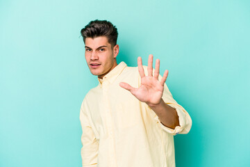 Young caucasian man isolated on blue background being shocked due to an imminent danger