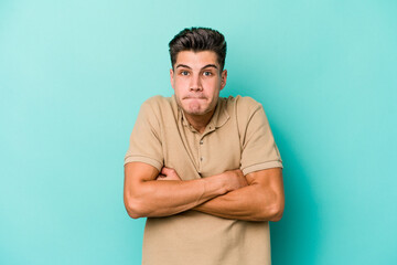 Fototapeta premium Young caucasian man isolated on blue background shrugs shoulders and open eyes confused.