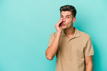 Young caucasian man isolated on blue background is saying a secret hot braking news and looking...