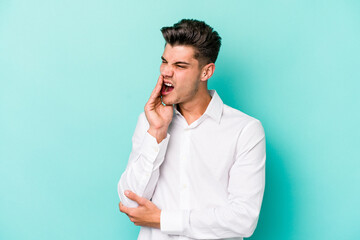 Young caucasian man isolated on blue background yawning showing a tired gesture covering mouth with hand.