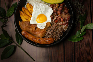 tray paisa aerial view, typical Colombian food, with beans, eggs, rice, pork rinds, avocado and chorizo ​​in plate on brown table