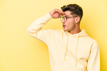 Young caucasian man isolated on yellow background looking far away keeping hand on forehead.