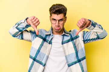 Young caucasian man isolated on yellow background showing a dislike gesture, thumbs down. Disagreement concept.