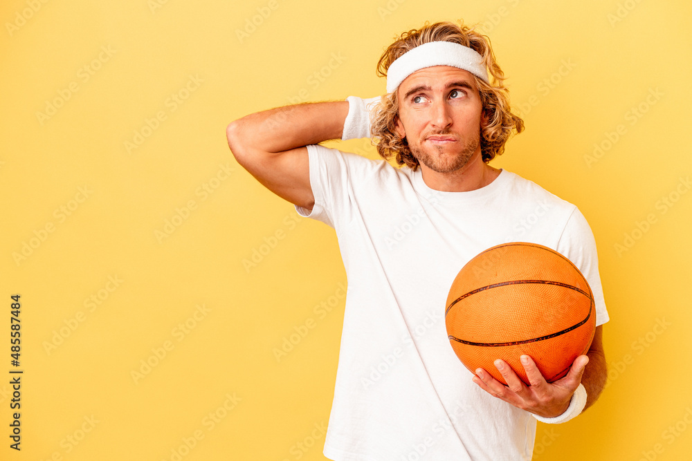 Wall mural young basketball player caucasian man isolated on yellow background touching back of head, thinking 