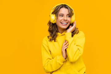 smiling attractive woman listening to music in headphones on yellow background
