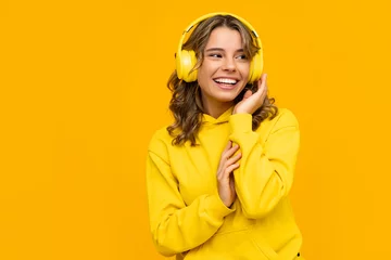 Fotobehang smiling attractive woman listening to music in headphones on yellow background © mary_markevich