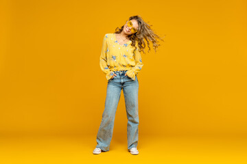 Fototapeta premium stylish happy smiling blond woman posing in jeans on yellow background