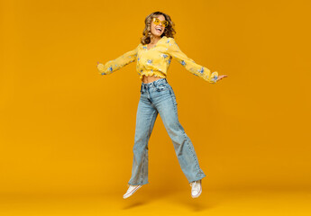 stylish happy smiling blond woman posing in jeans on yellow background