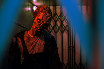 Waist up shot of gory zombie looking at camera in dark hallway lit by red light, copy space