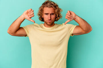 Young caucasian man isolated on blue background showing a dislike gesture, thumbs down....