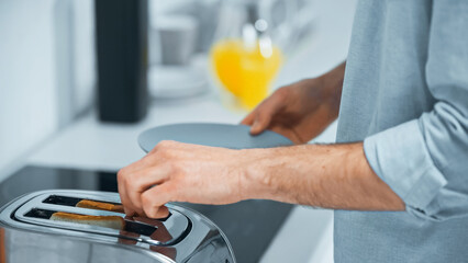 cropped view of man preparing toasts in electric toaster in kitchen