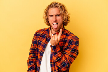 Young caucasian man isolated on yellow background showing rock gesture with fingers