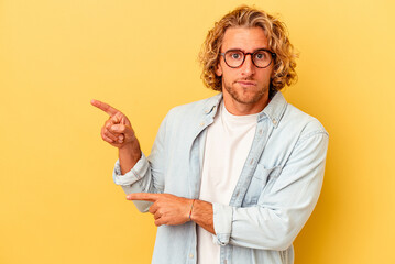 Young caucasian man isolated on yellow background shocked pointing with index fingers to a copy...
