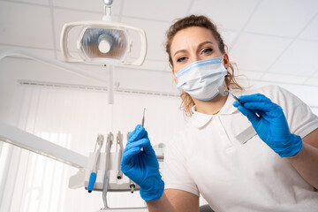 Fototapeta na wymiar Dentist woman alone holding dental instruments, looking at the camera. Personal or patient point of view, POV. dental treatment concept.