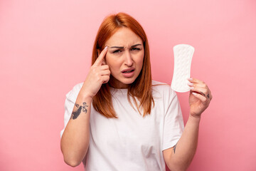 Young caucasian woman holding sanitary napkin isolated on pink background showing a disappointment gesture with forefinger.