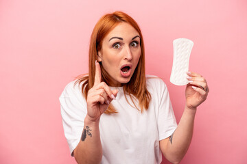 Young caucasian woman holding sanitary napkin isolated on pink background having an idea, inspiration concept.