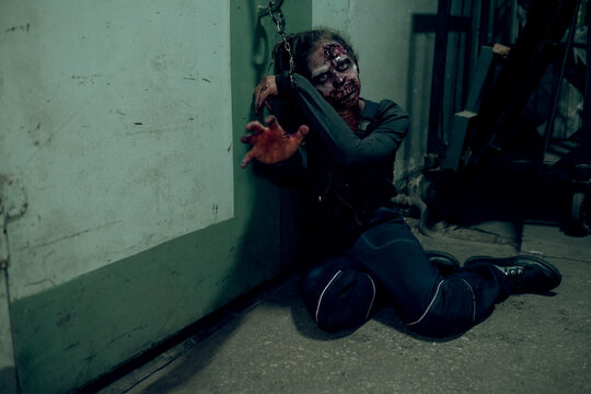 Full length shot of female zombie chained to wall in dark room and reaching to camera, copy space