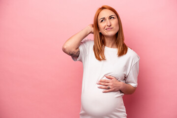 Young caucasian pregnant woman isolated on pink background touching back of head, thinking and...